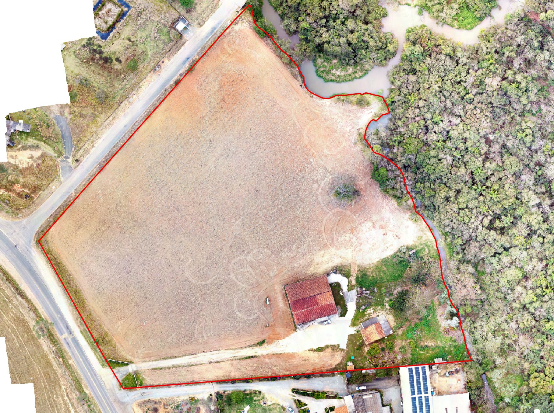 Ortomosaico aéreo gerado por drone com delimitação da área em vermelho, mata ciliar e curso d'água